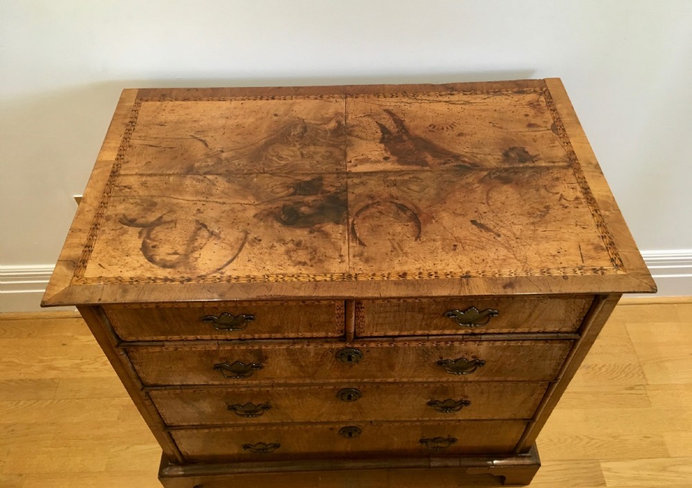 An eighteenth-century walnut chest of drawers featuring decorative poker work inlay, brass swing handles, keyhole escutcheons, and straight bracket feet. View II