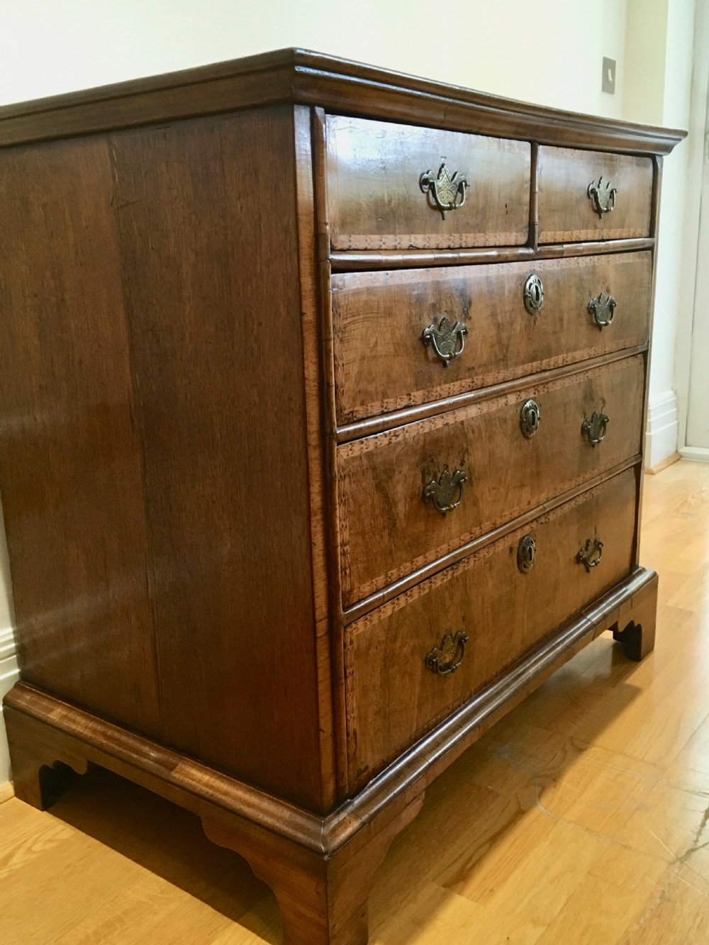 An eighteenth-century walnut chest of drawers featuring decorative poker work inlay, brass swing handles, keyhole escutcheons, and straight bracket feet. View IV