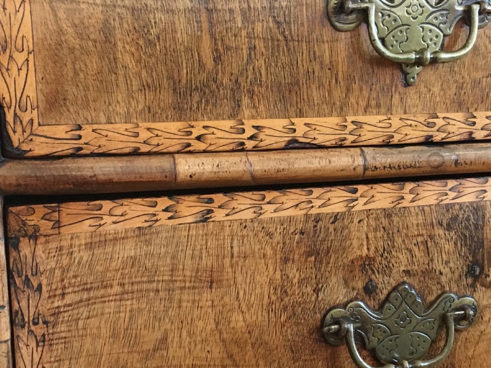 An eighteenth-century walnut chest of drawers featuring decorative poker work inlay, brass swing handles, keyhole escutcheons, and straight bracket feet. View V