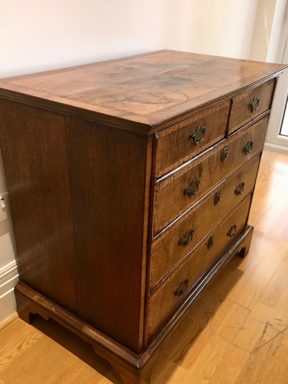 An eighteenth-century walnut chest of drawers featuring decorative poker work inlay, brass swing handles, keyhole escutcheons, and straight bracket feet. View X
