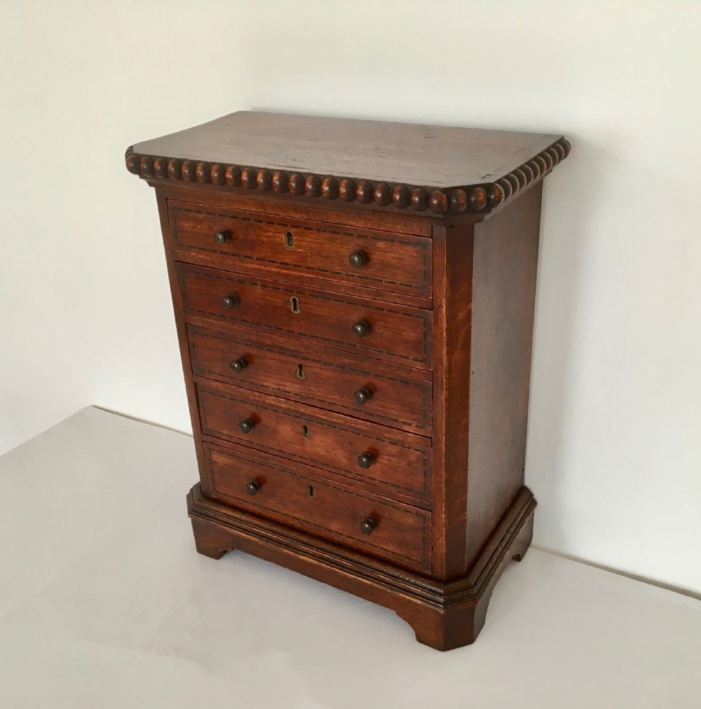 A small dark oak tabletop collectors cabinet featuring five inlaid drawers, turned wooden knobs, and a carved beaded top edge. View II