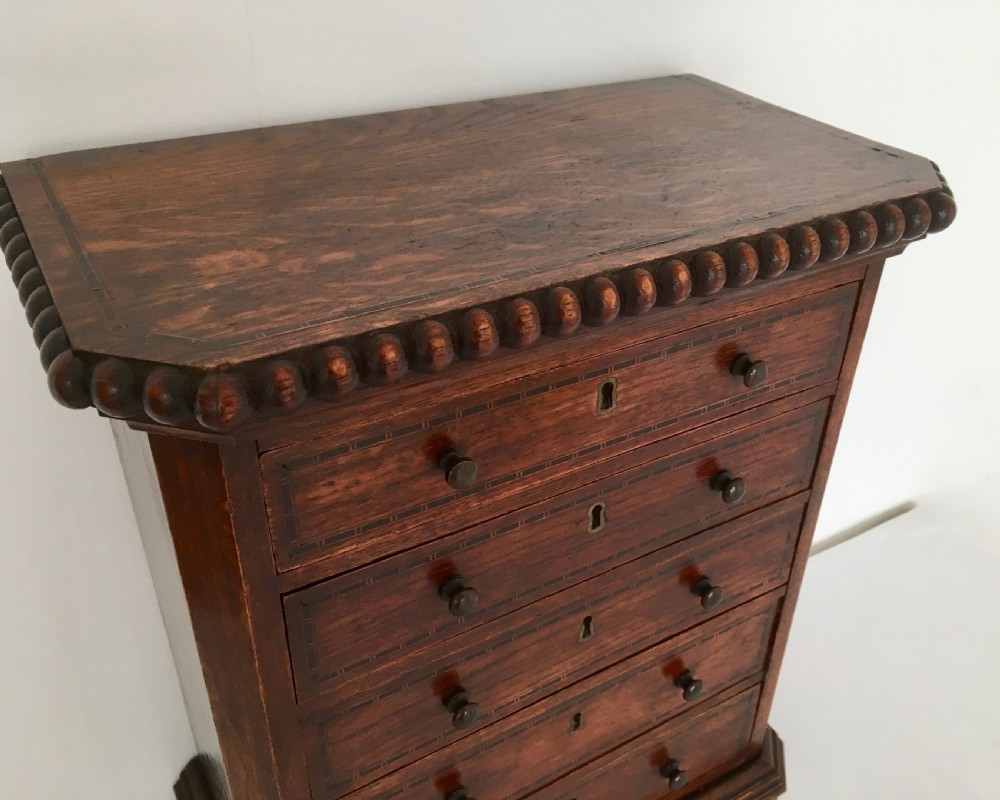 A small dark oak tabletop collectors cabinet featuring five inlaid drawers, turned wooden knobs, and a carved beaded top edge. View III