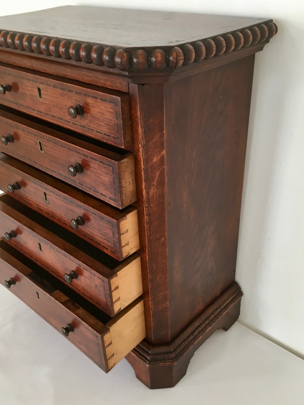 A small dark oak tabletop collectors cabinet featuring five inlaid drawers, turned wooden knobs, and a carved beaded top edge. View IV