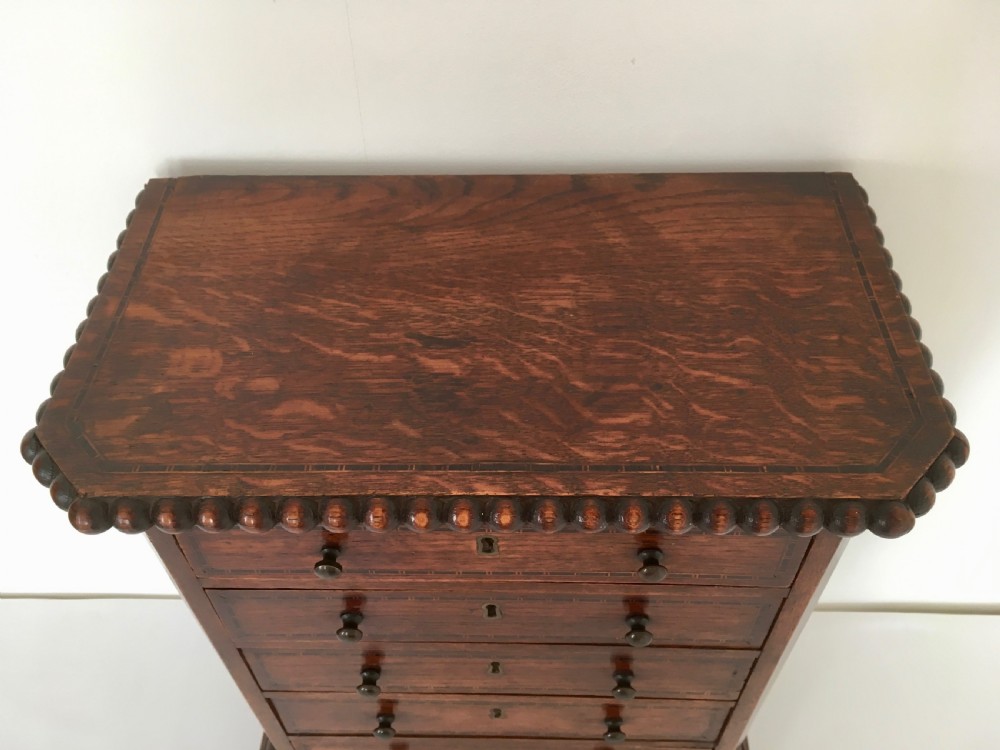A small dark oak tabletop collectors cabinet featuring five inlaid drawers, turned wooden knobs, and a carved beaded top edge. View VI