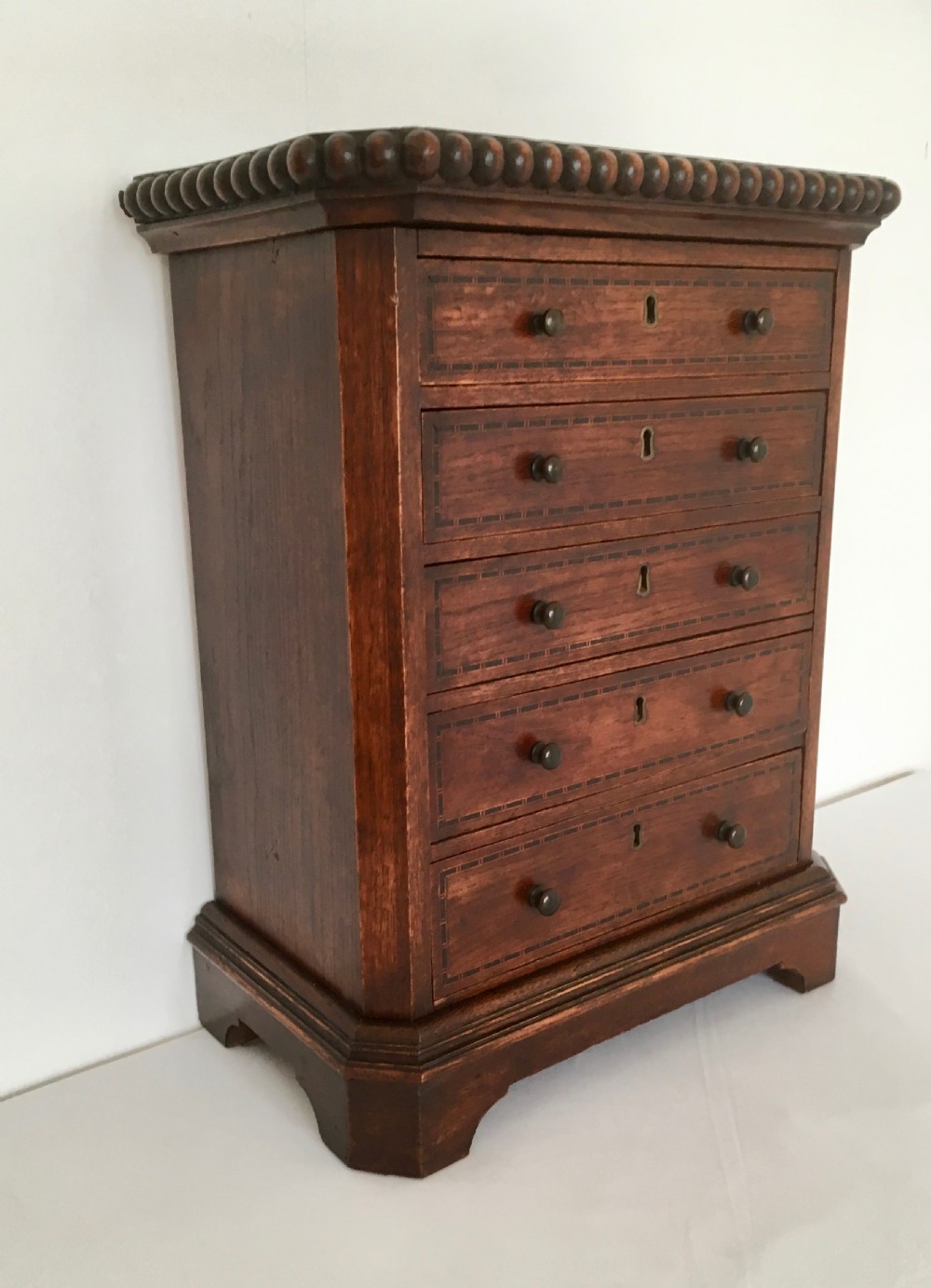A small dark oak tabletop collectors cabinet featuring five inlaid drawers, turned wooden knobs, and a carved beaded top edge. View VIII