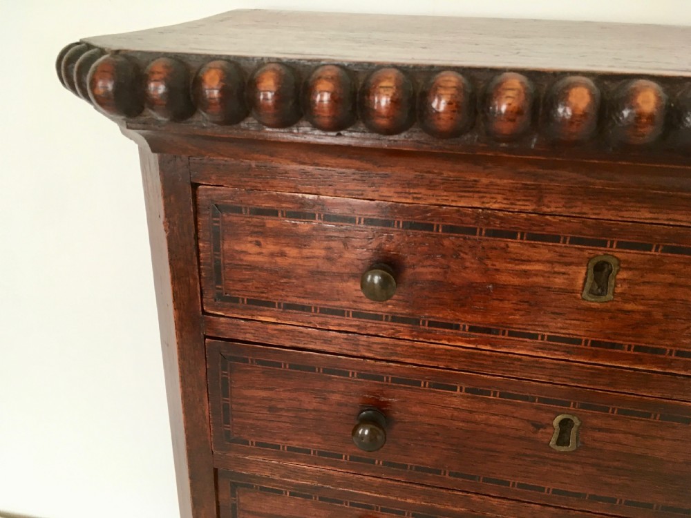 A small dark oak tabletop collectors cabinet featuring five inlaid drawers, turned wooden knobs, and a carved beaded top edge. View IX