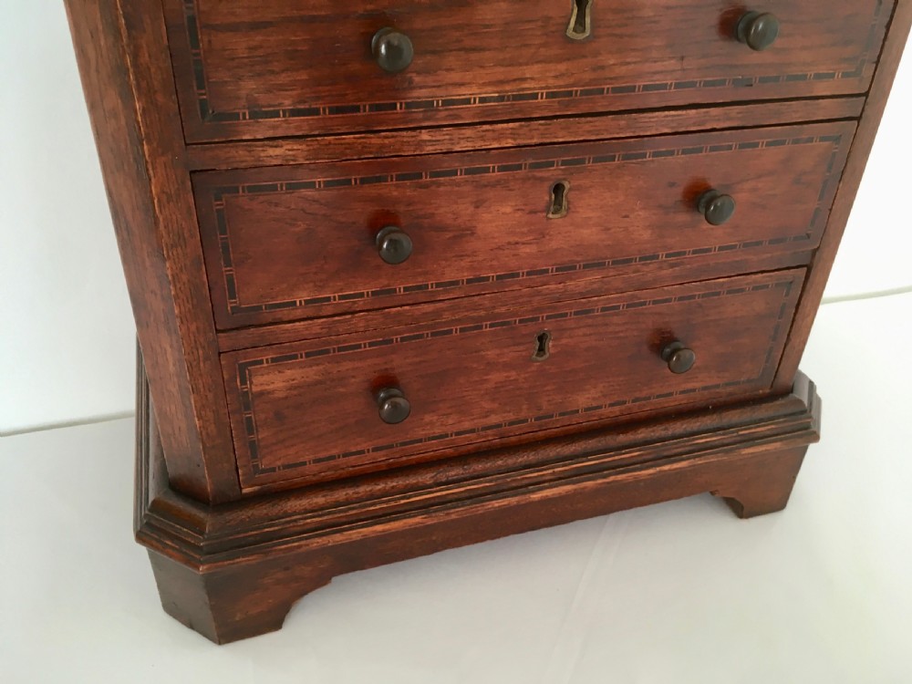 A small dark oak tabletop collectors cabinet featuring five inlaid drawers, turned wooden knobs, and a carved beaded top edge. View X