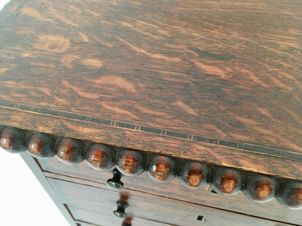 A small dark oak tabletop collectors cabinet featuring five inlaid drawers, turned wooden knobs, and a carved beaded top edge. View XI
