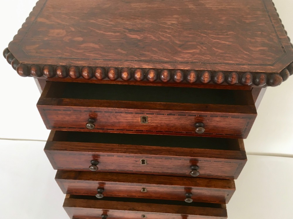 A small dark oak tabletop collectors cabinet featuring five inlaid drawers, turned wooden knobs, and a carved beaded top edge. View XIII