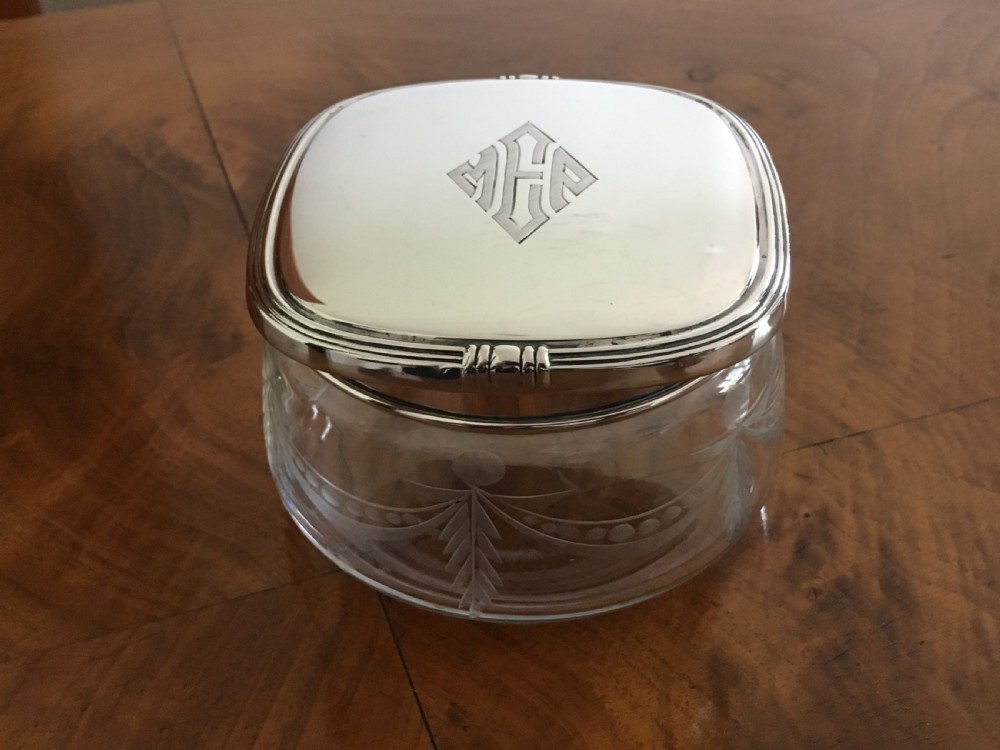 A five-piece silver Art Deco dressing table set featuring a hand mirror, brushes, and a silver-topped glass pot, each detailed with geometric engraved monograms. View III