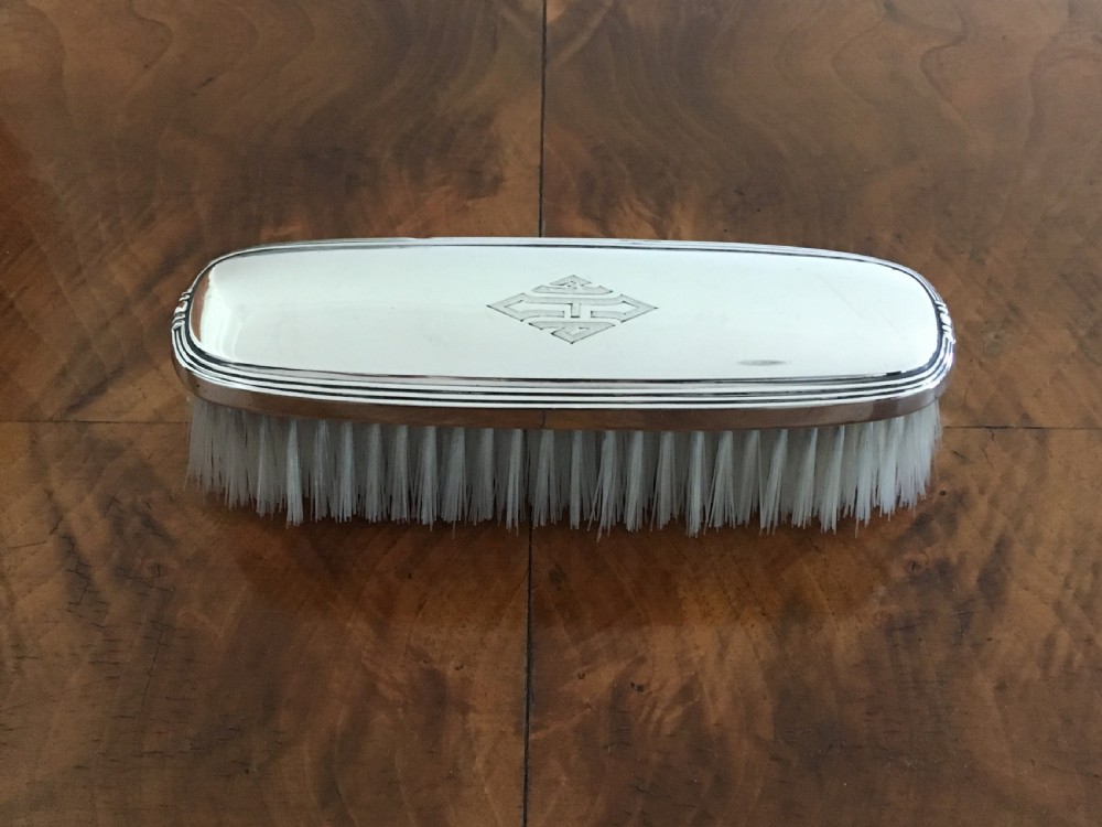 A five-piece silver Art Deco dressing table set featuring a hand mirror, brushes, and a silver-topped glass pot, each detailed with geometric engraved monograms. View IV
