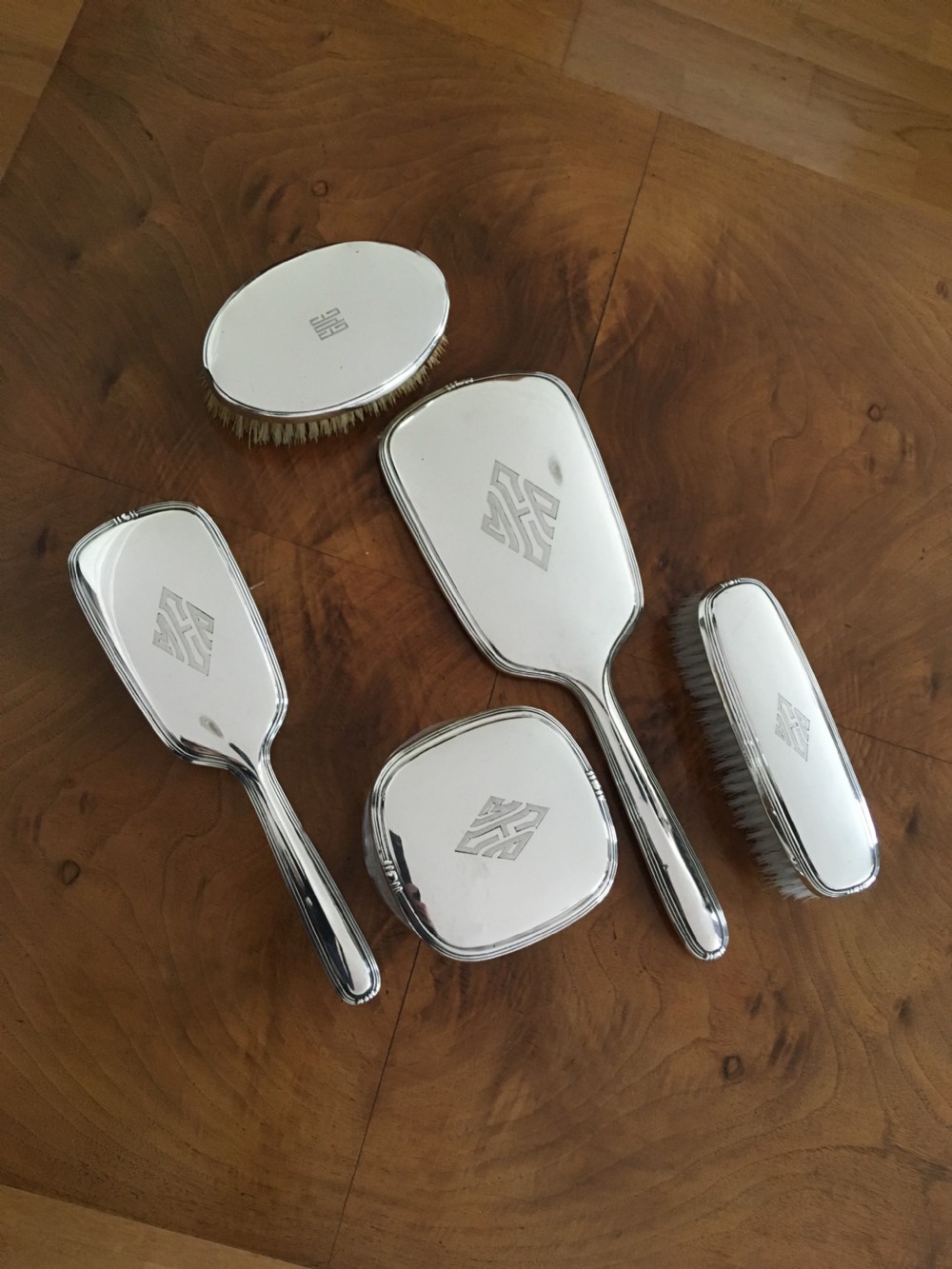 A five-piece silver Art Deco dressing table set featuring a hand mirror, brushes, and a silver-topped glass pot, each detailed with geometric engraved monograms. View IX