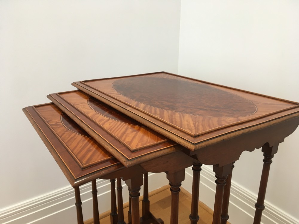 A set of three nested wooden side tables featuring rectangular tops with oval amboyna wood centres, inlaid satinwood borders, and slender turned legs. View X