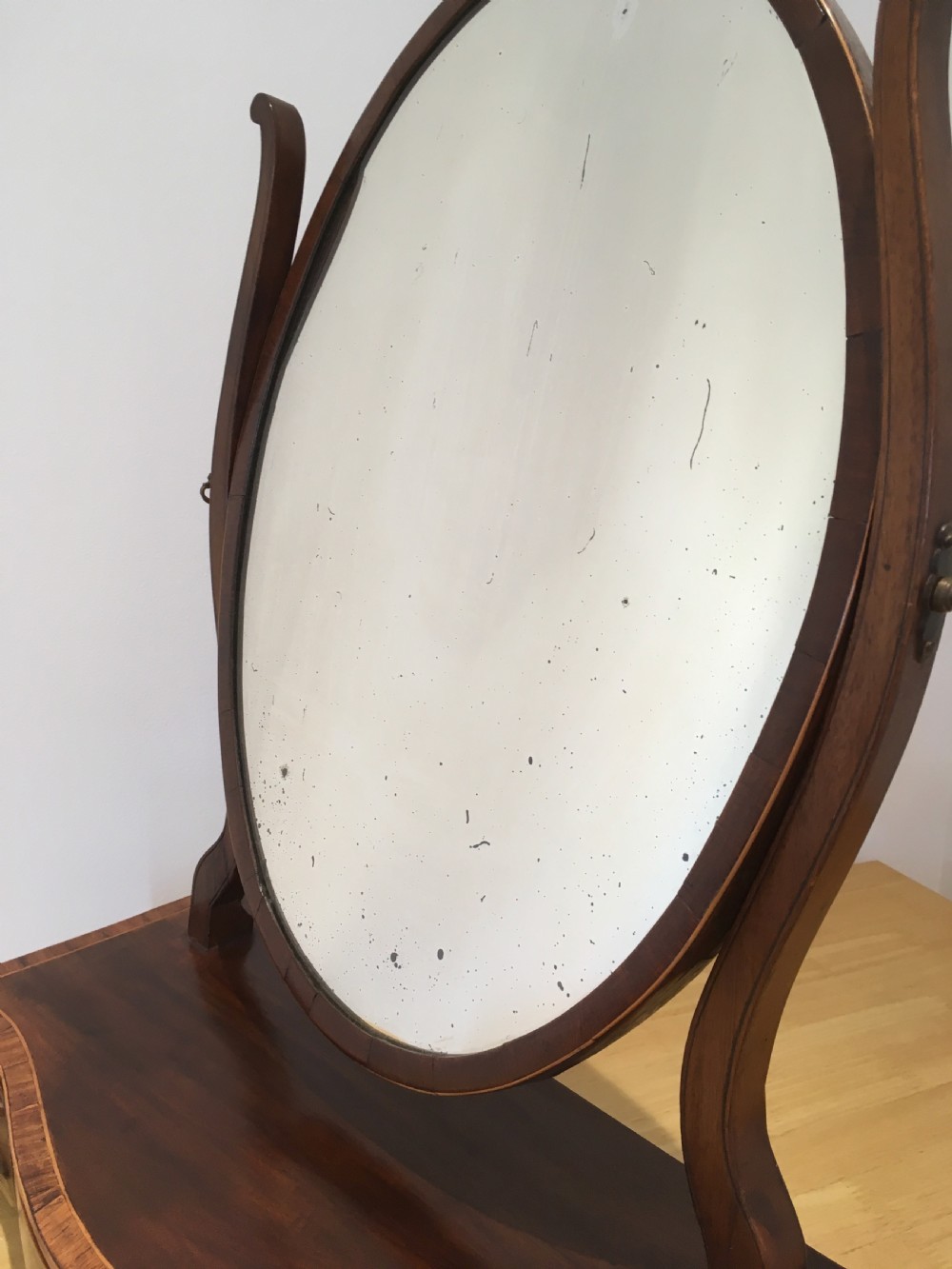An antique Georgian mahogany toilet mirror with an oval pivoting mirror above a serpentine base fitted with three small drawers and light-coloured knobs. View VI