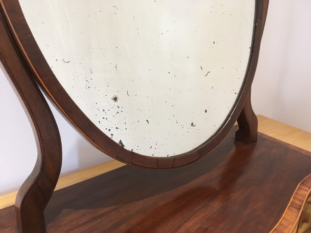 An antique Georgian mahogany toilet mirror with an oval pivoting mirror above a serpentine base fitted with three small drawers and light-coloured knobs. View VIII