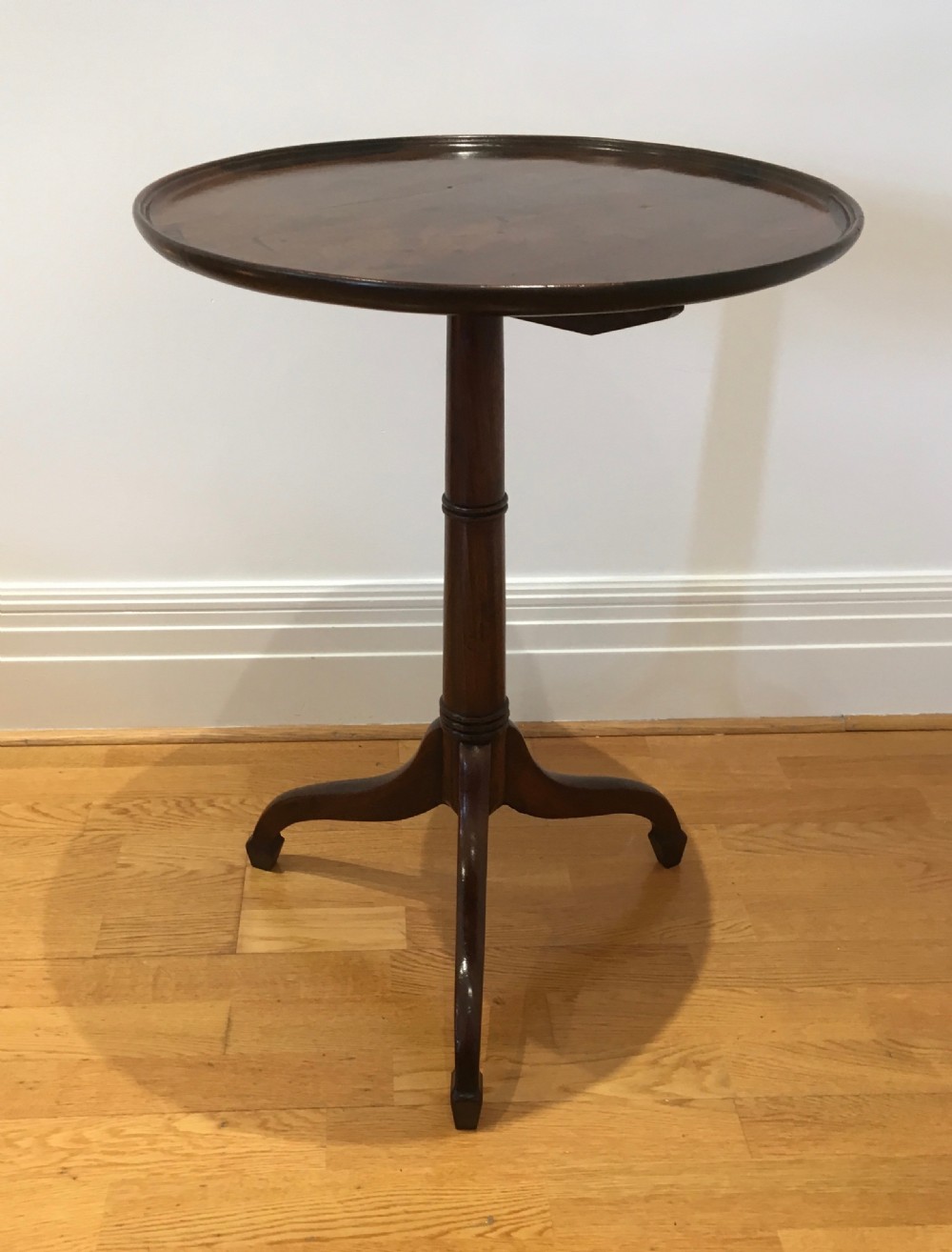 A Georgian dark mahogany tilt-top occasional table featuring a circular dished top supported by a turned central pedestal column and a tripod base with downswept legs.