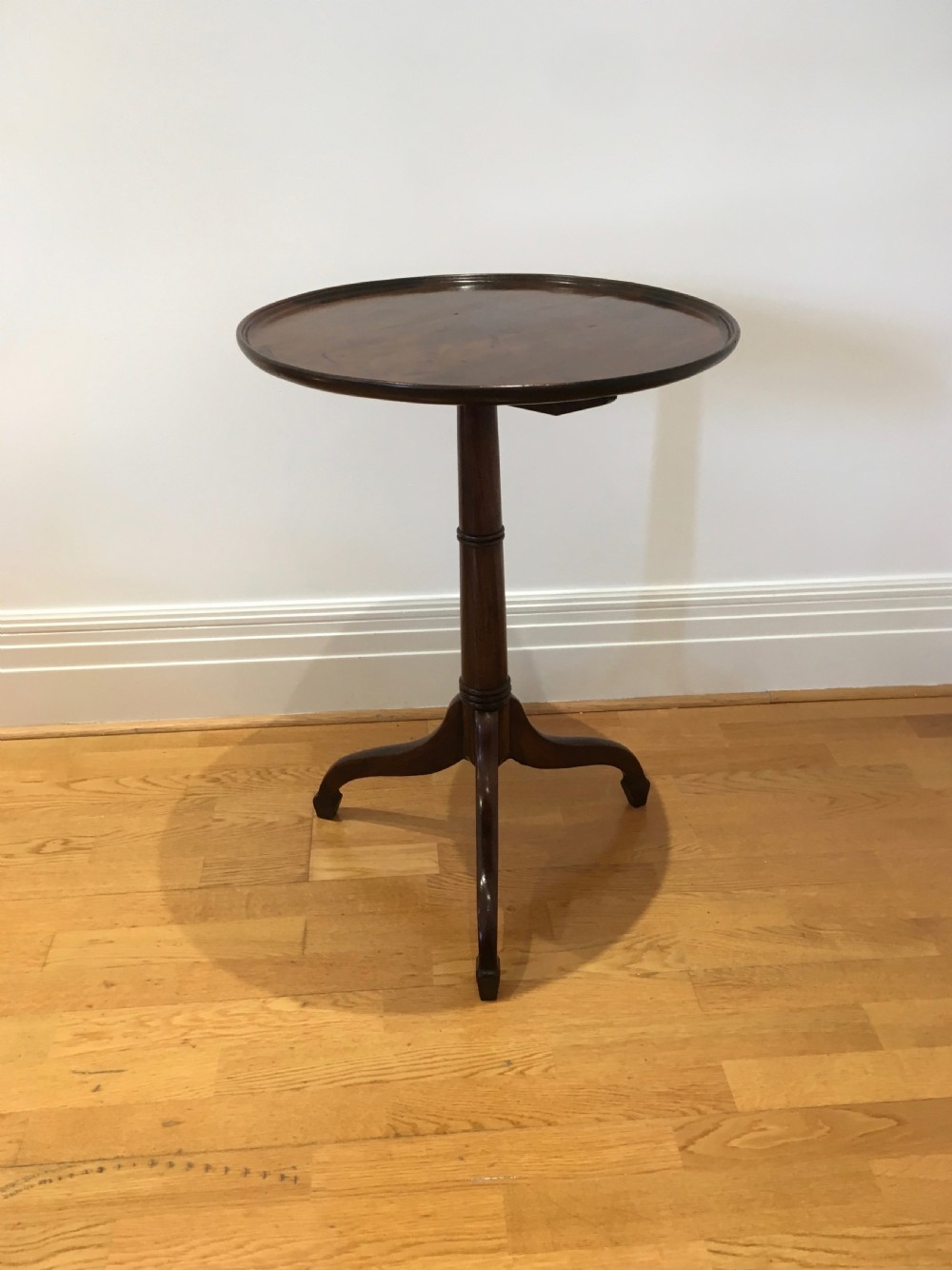 A Georgian dark mahogany tilt-top occasional table featuring a circular dished top supported by a turned central pedestal column and a tripod base with downswept legs. View II