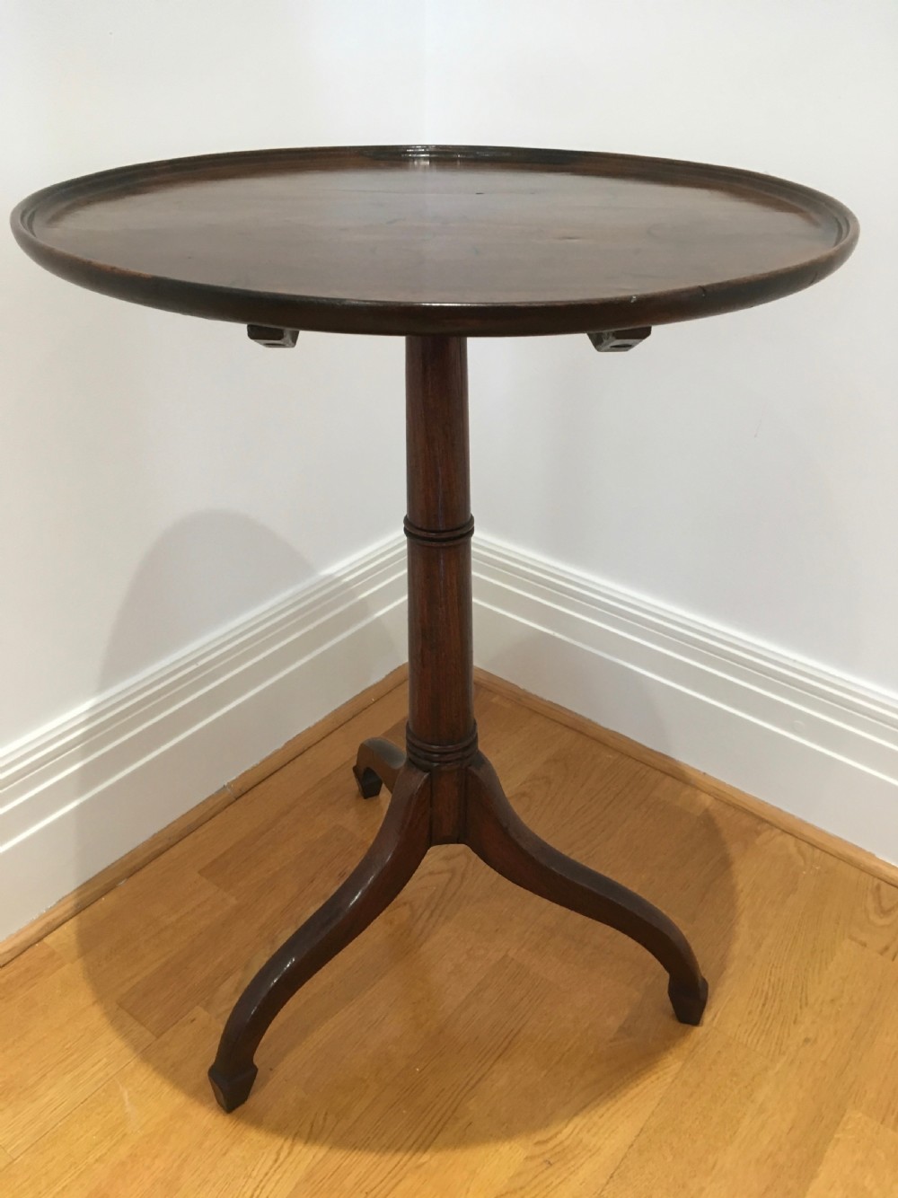 A Georgian dark mahogany tilt-top occasional table featuring a circular dished top supported by a turned central pedestal column and a tripod base with downswept legs. View V