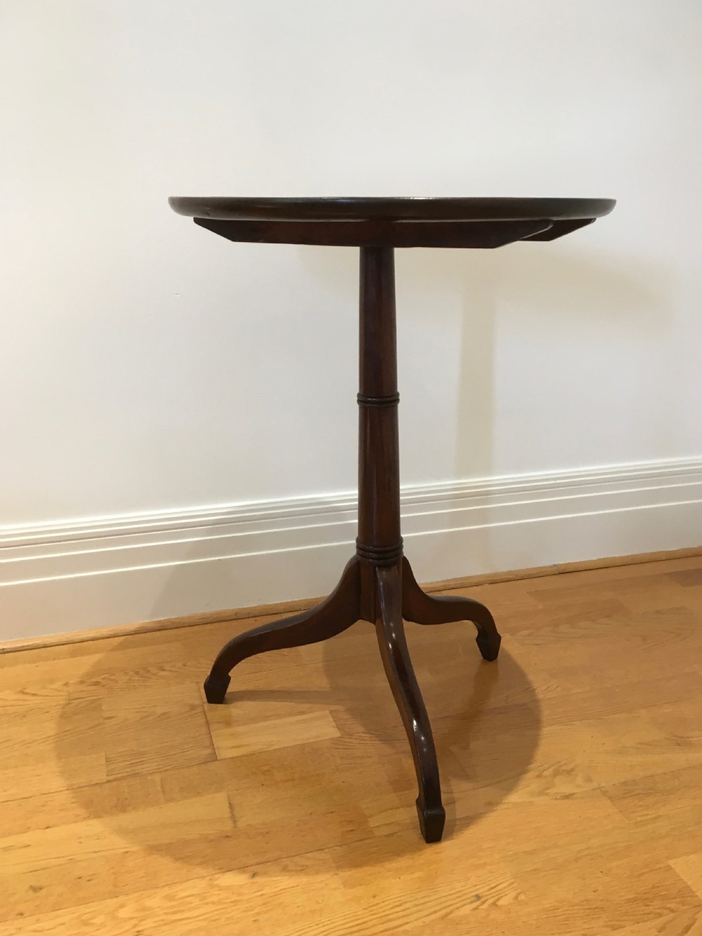 A Georgian dark mahogany tilt-top occasional table featuring a circular dished top supported by a turned central pedestal column and a tripod base with downswept legs. View VII