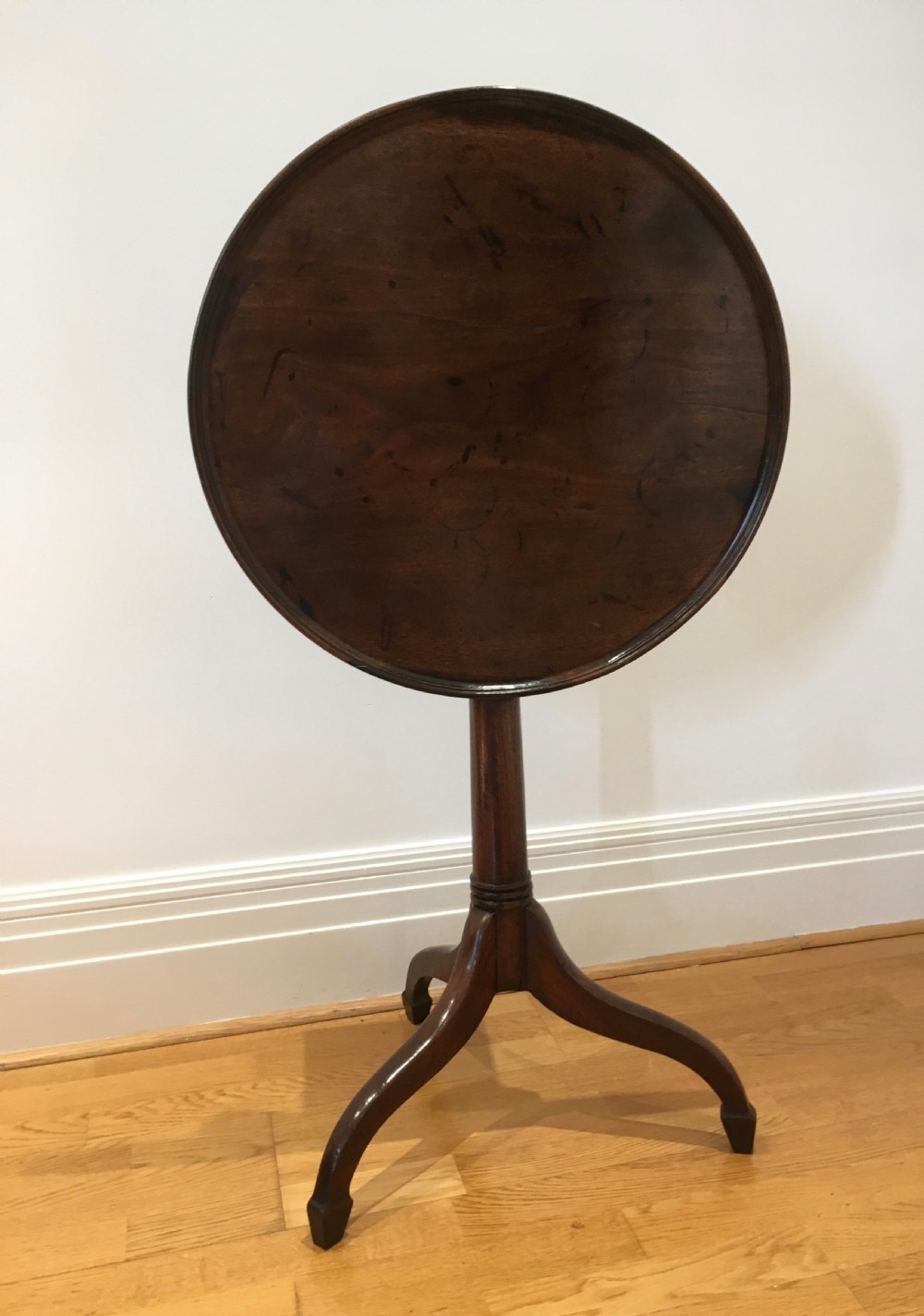 A Georgian dark mahogany tilt-top occasional table featuring a circular dished top supported by a turned central pedestal column and a tripod base with downswept legs. View X