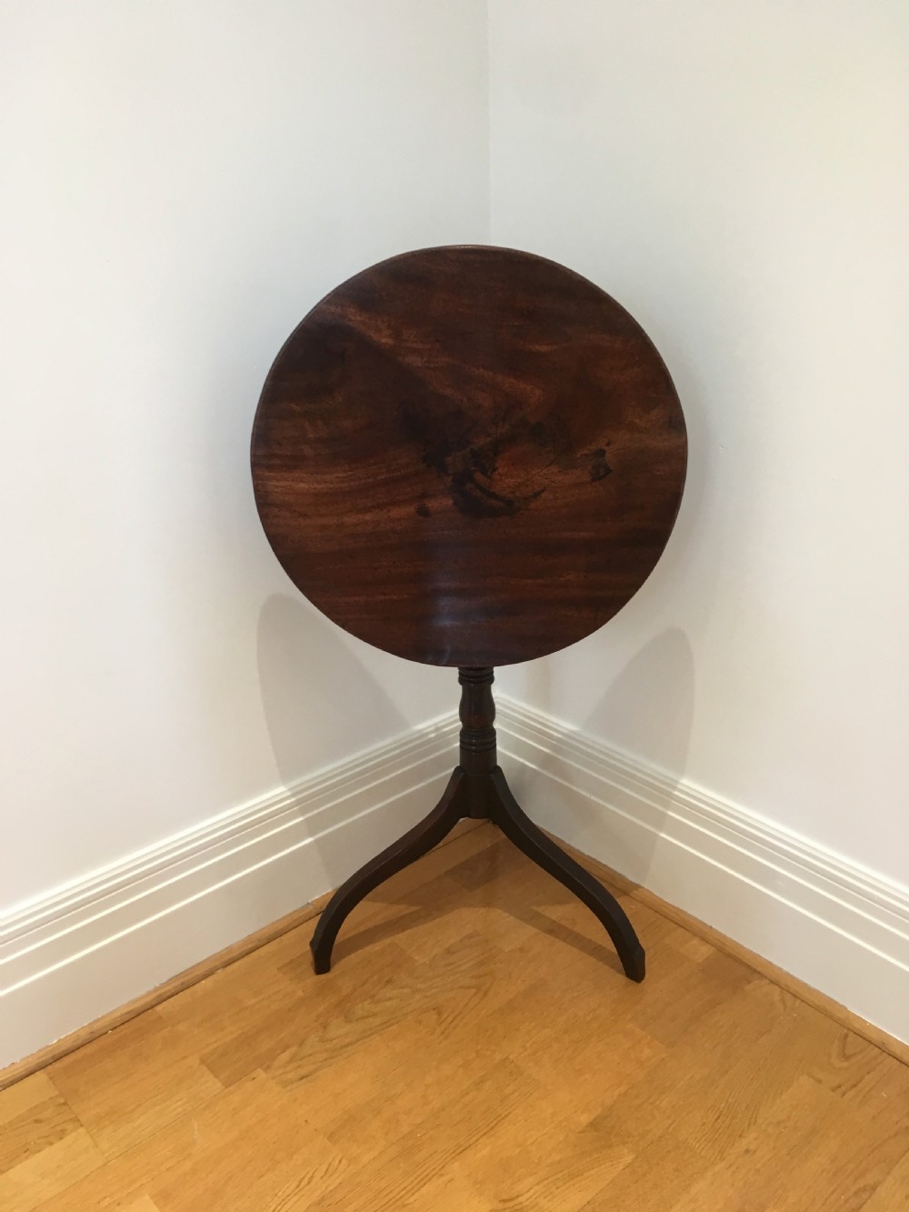 A Georgian mahogany tilt-top table with a circular top locked in a vertical position on a turned central pedestal with three down-swept legs.