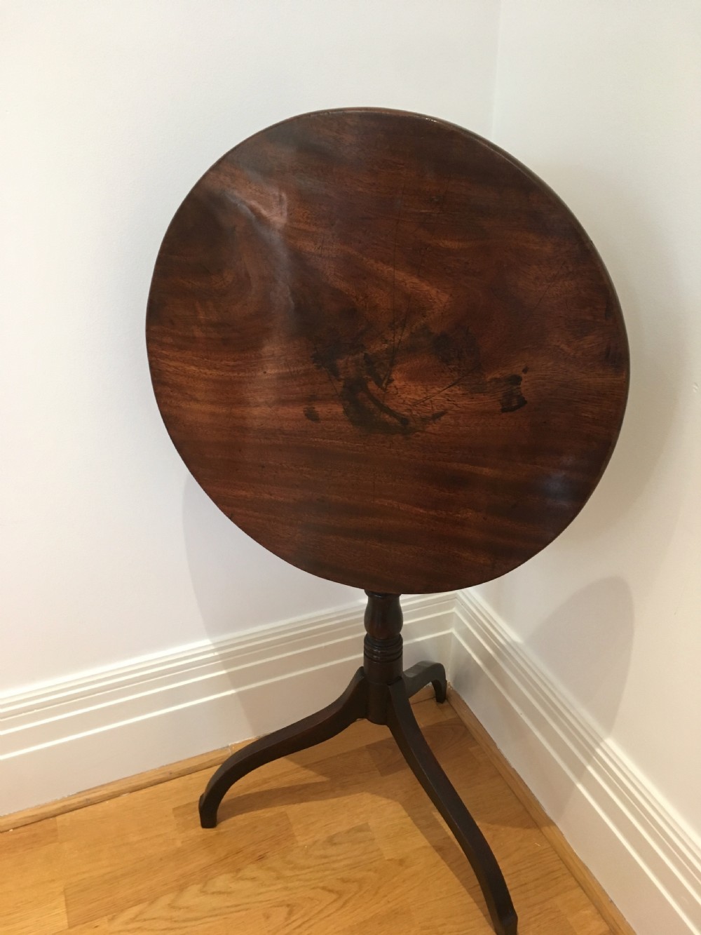 A Georgian mahogany tilt-top table with a circular top locked in a vertical position on a turned central pedestal with three down-swept legs. View II