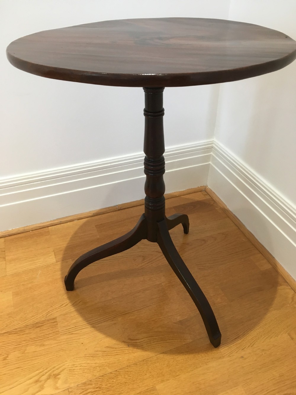 A Georgian mahogany tilt-top table with a circular top locked in a vertical position on a turned central pedestal with three down-swept legs. View IV