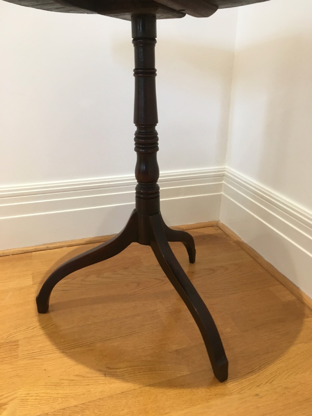 A Georgian mahogany tilt-top table with a circular top locked in a vertical position on a turned central pedestal with three down-swept legs. View V