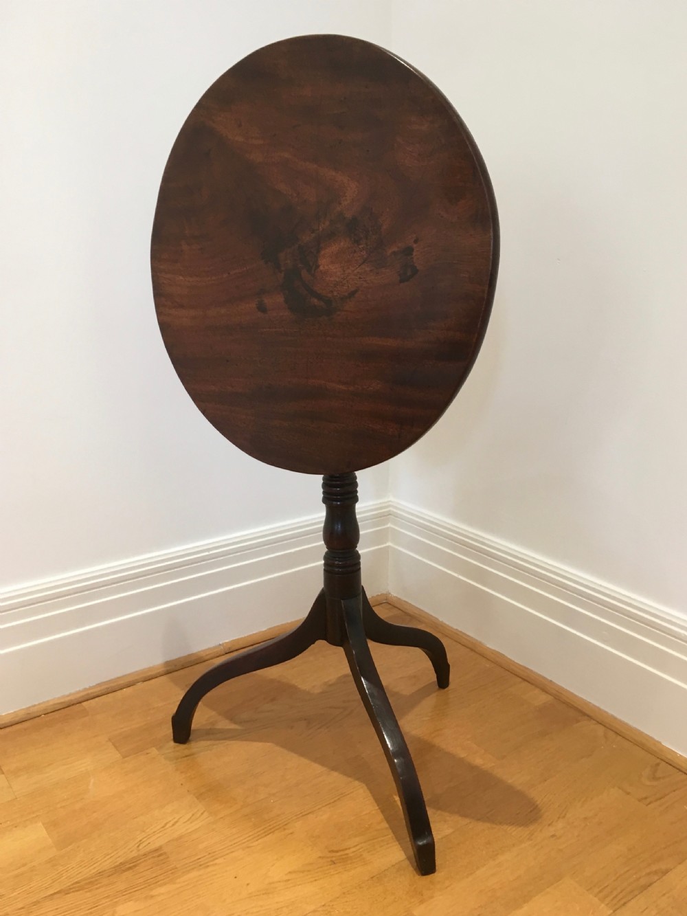 A Georgian mahogany tilt-top table with a circular top locked in a vertical position on a turned central pedestal with three down-swept legs. View XI