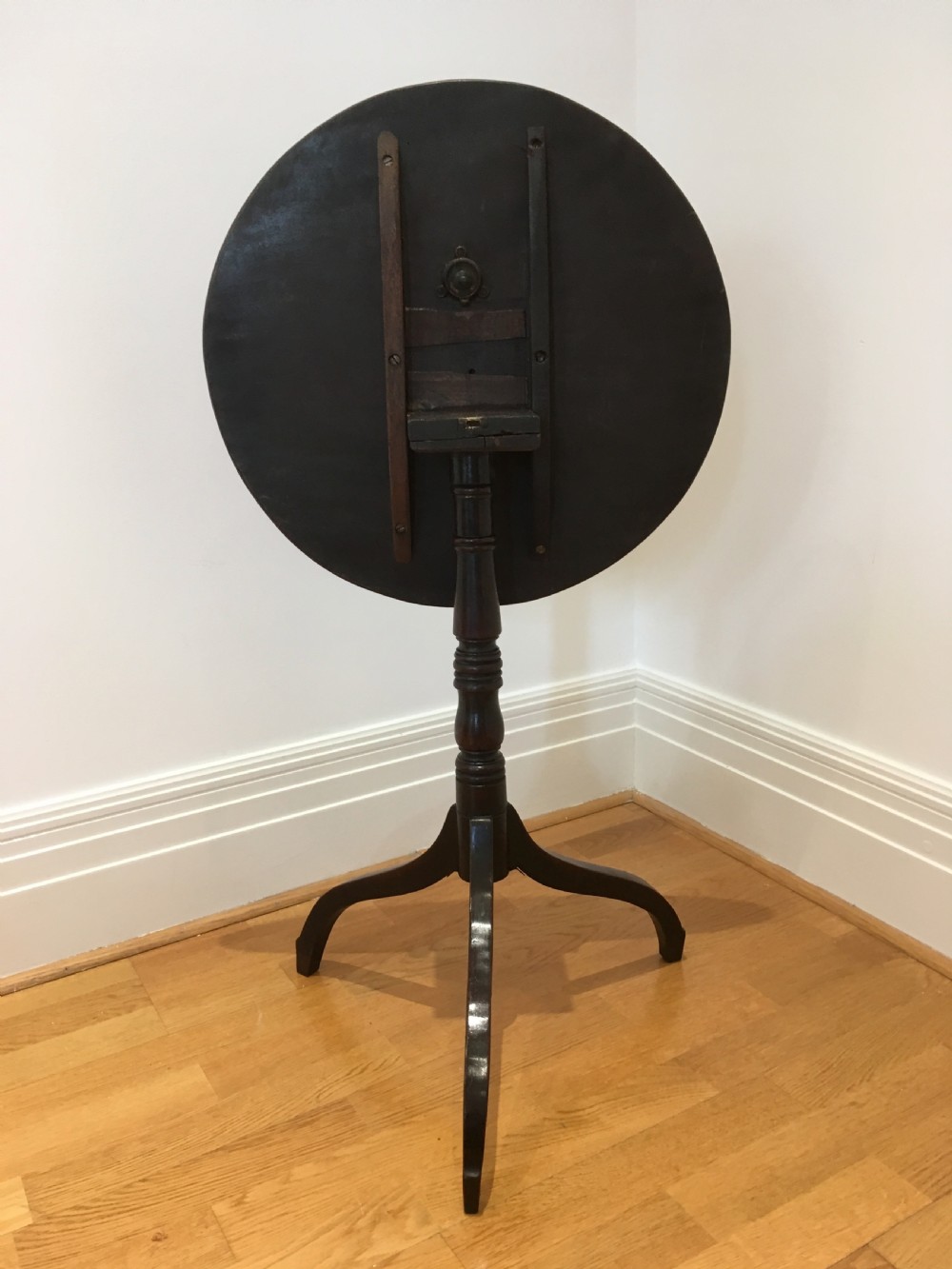 A Georgian mahogany tilt-top table with a circular top locked in a vertical position on a turned central pedestal with three down-swept legs. View XII
