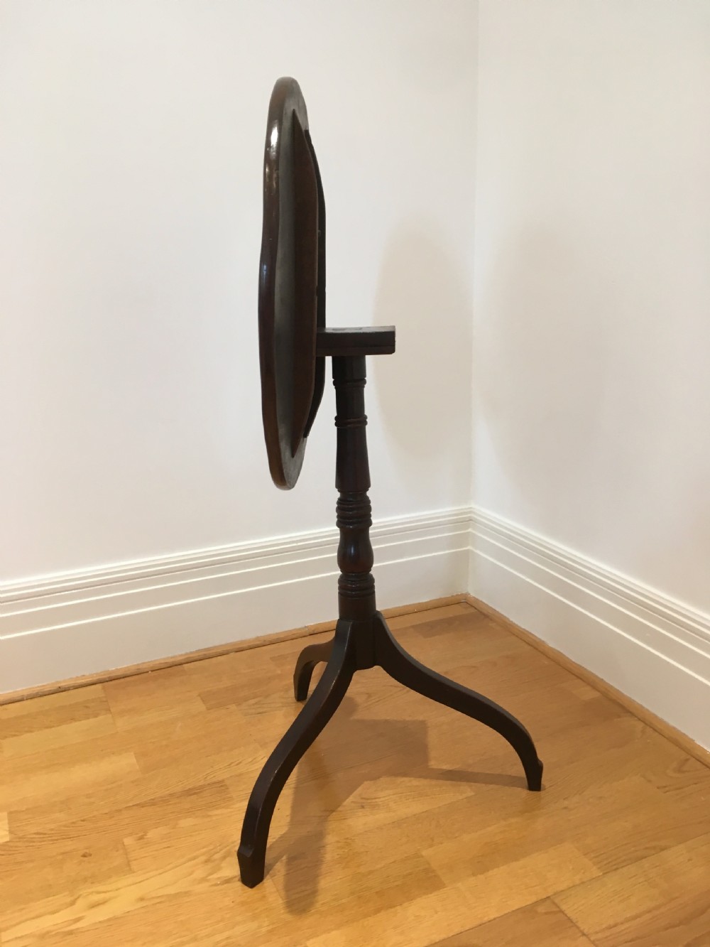 A Georgian mahogany tilt-top table with a circular top locked in a vertical position on a turned central pedestal with three down-swept legs. View XIII