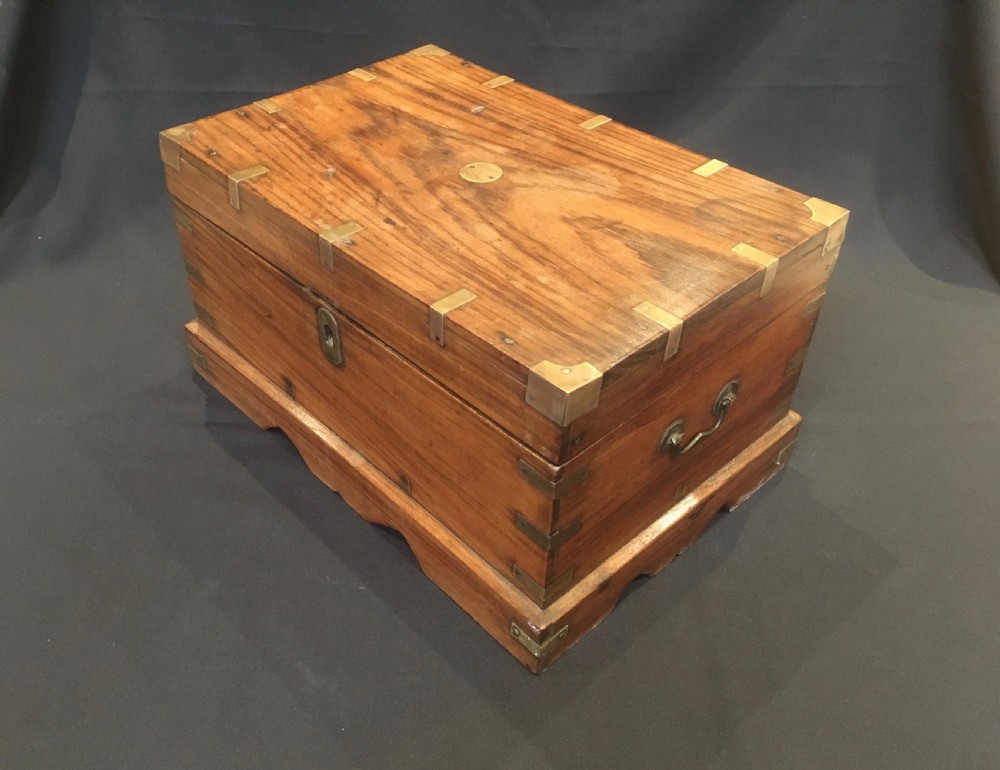 A rectangular warm brown oak desk box featuring brass bound corners, metal straps, a central brass oval cartouche, and a front keyhole escutcheon. View II