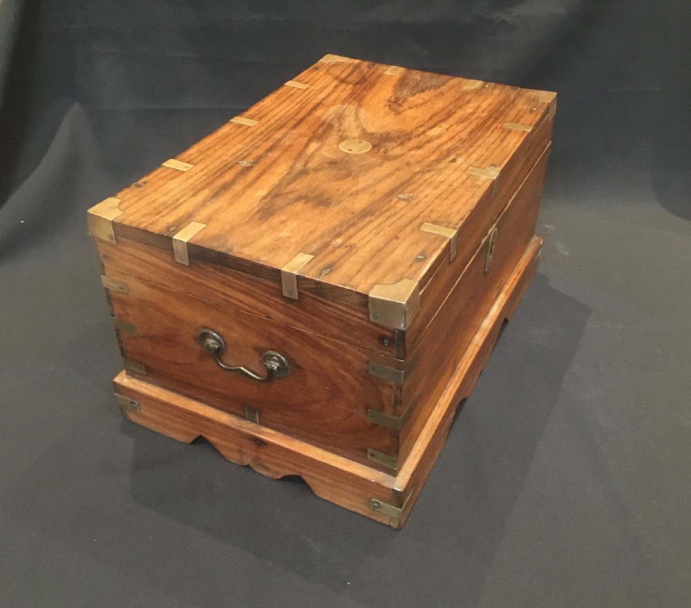 A rectangular warm brown oak desk box featuring brass bound corners, metal straps, a central brass oval cartouche, and a front keyhole escutcheon. View III
