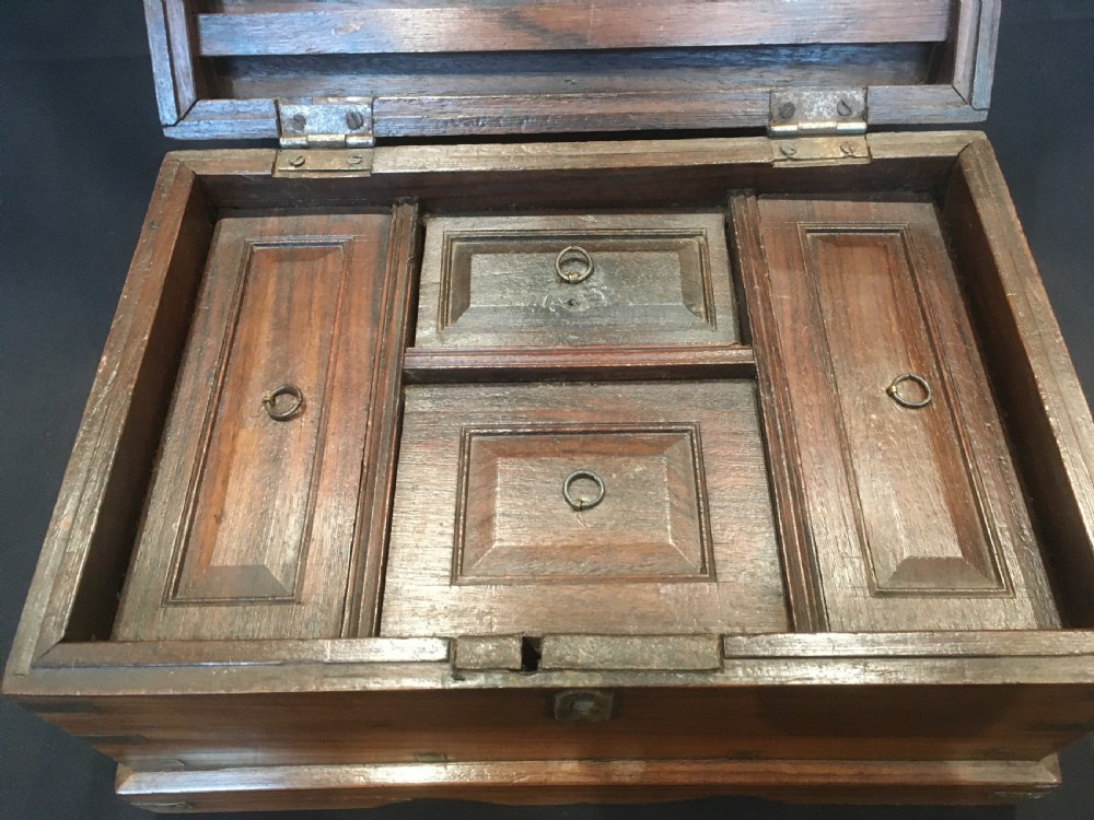 A rectangular warm brown oak desk box featuring brass bound corners, metal straps, a central brass oval cartouche, and a front keyhole escutcheon. View V