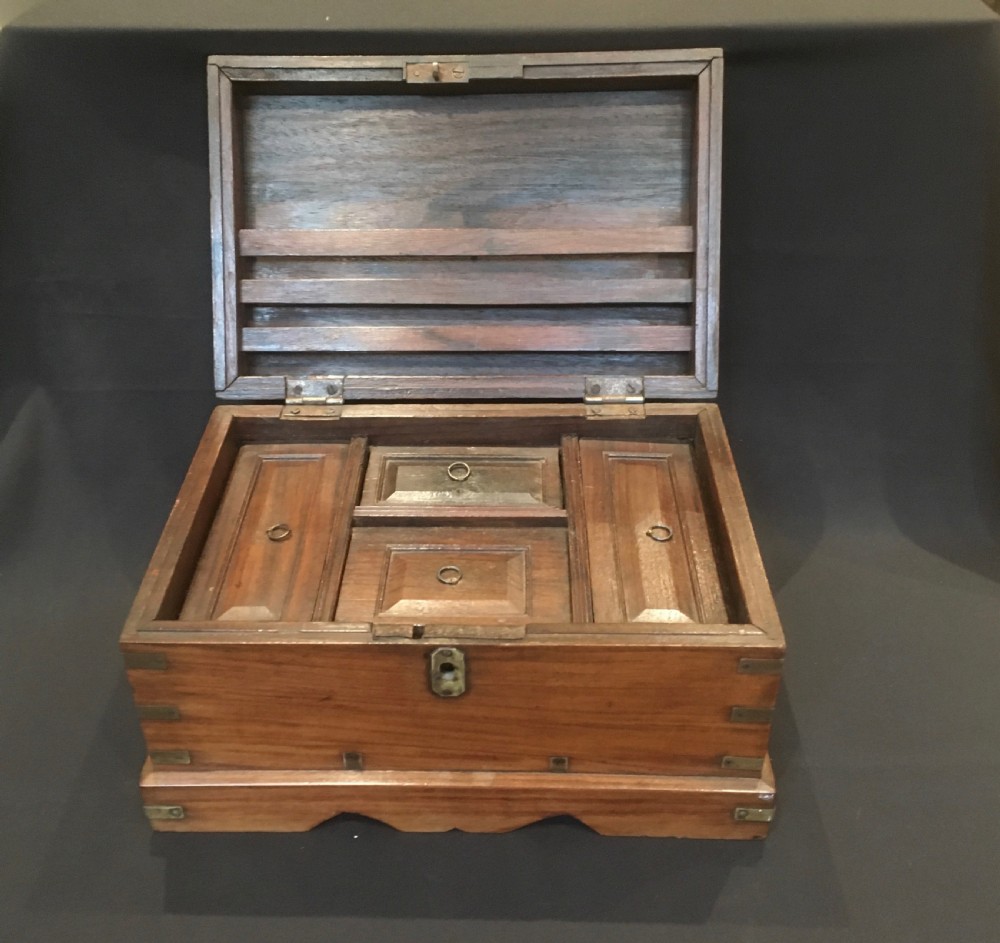 A rectangular warm brown oak desk box featuring brass bound corners, metal straps, a central brass oval cartouche, and a front keyhole escutcheon. View X