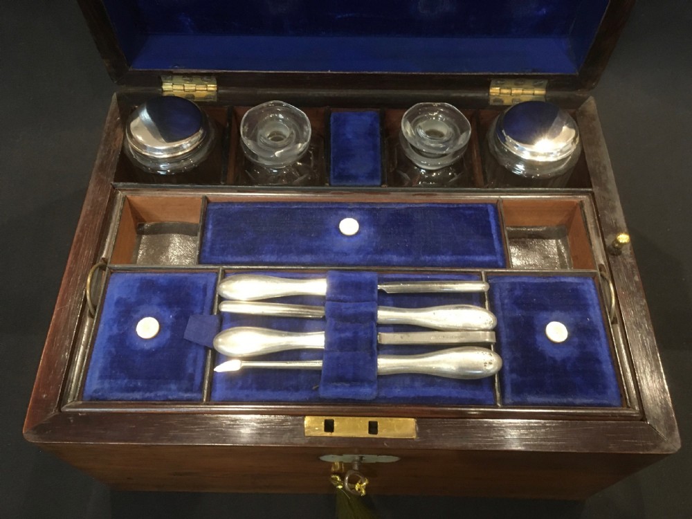 An open rosewood vanity box lined with vibrant blue velvet, containing cut glass jars, silver-plated lids, and manicure tools. View III