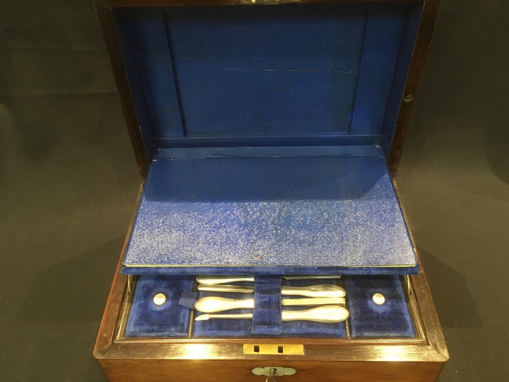 An open rosewood vanity box lined with vibrant blue velvet, containing cut glass jars, silver-plated lids, and manicure tools. View IV