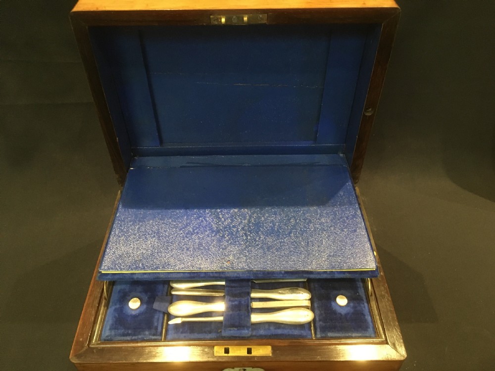 An open rosewood vanity box lined with vibrant blue velvet, containing cut glass jars, silver-plated lids, and manicure tools. View V