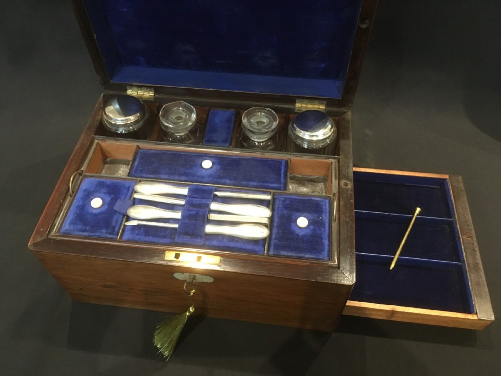 An open rosewood vanity box lined with vibrant blue velvet, containing cut glass jars, silver-plated lids, and manicure tools. View VI