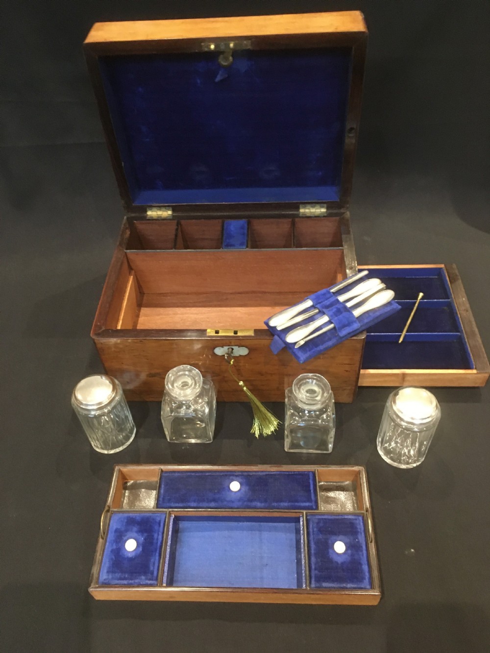 An open rosewood vanity box lined with vibrant blue velvet, containing cut glass jars, silver-plated lids, and manicure tools. View VII