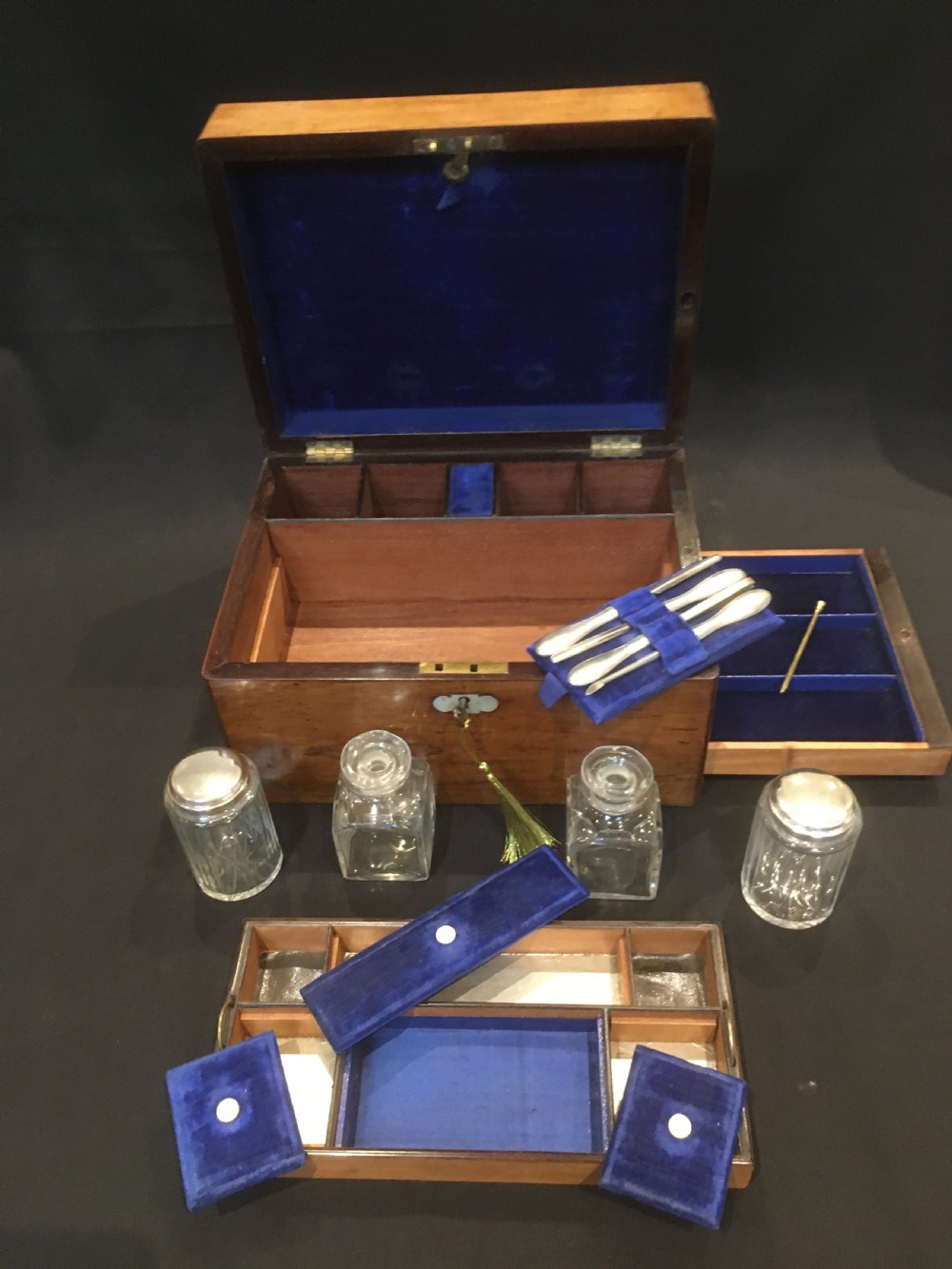 An open rosewood vanity box lined with vibrant blue velvet, containing cut glass jars, silver-plated lids, and manicure tools. View VIII