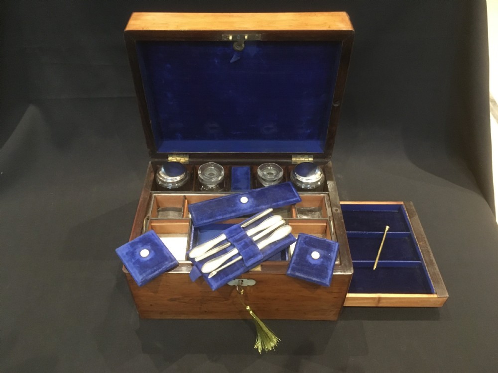 An open rosewood vanity box lined with vibrant blue velvet, containing cut glass jars, silver-plated lids, and manicure tools. View IX