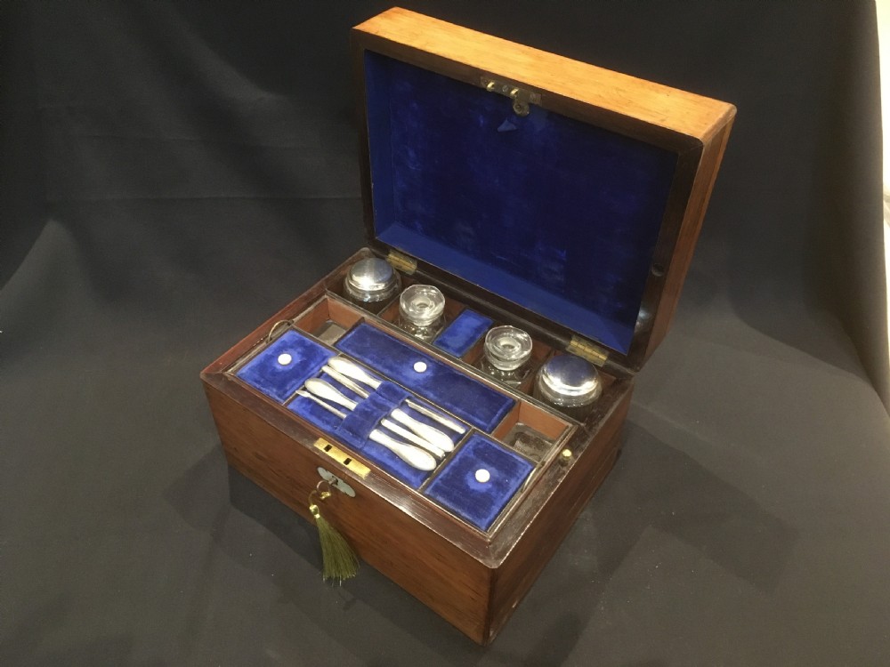 An open rosewood vanity box lined with vibrant blue velvet, containing cut glass jars, silver-plated lids, and manicure tools. View X