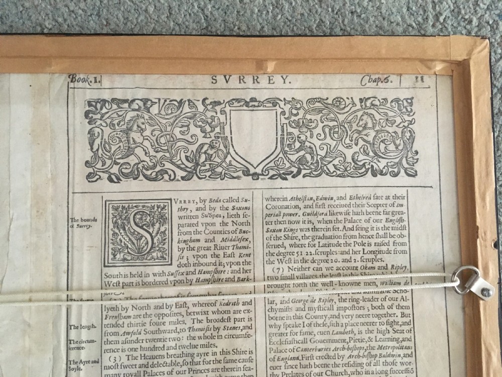 A framed historical map of Surrey by John Speed, displaying administrative divisions, coats of arms, and detailed corner insets of Richmond and Nonsuch palaces. View X