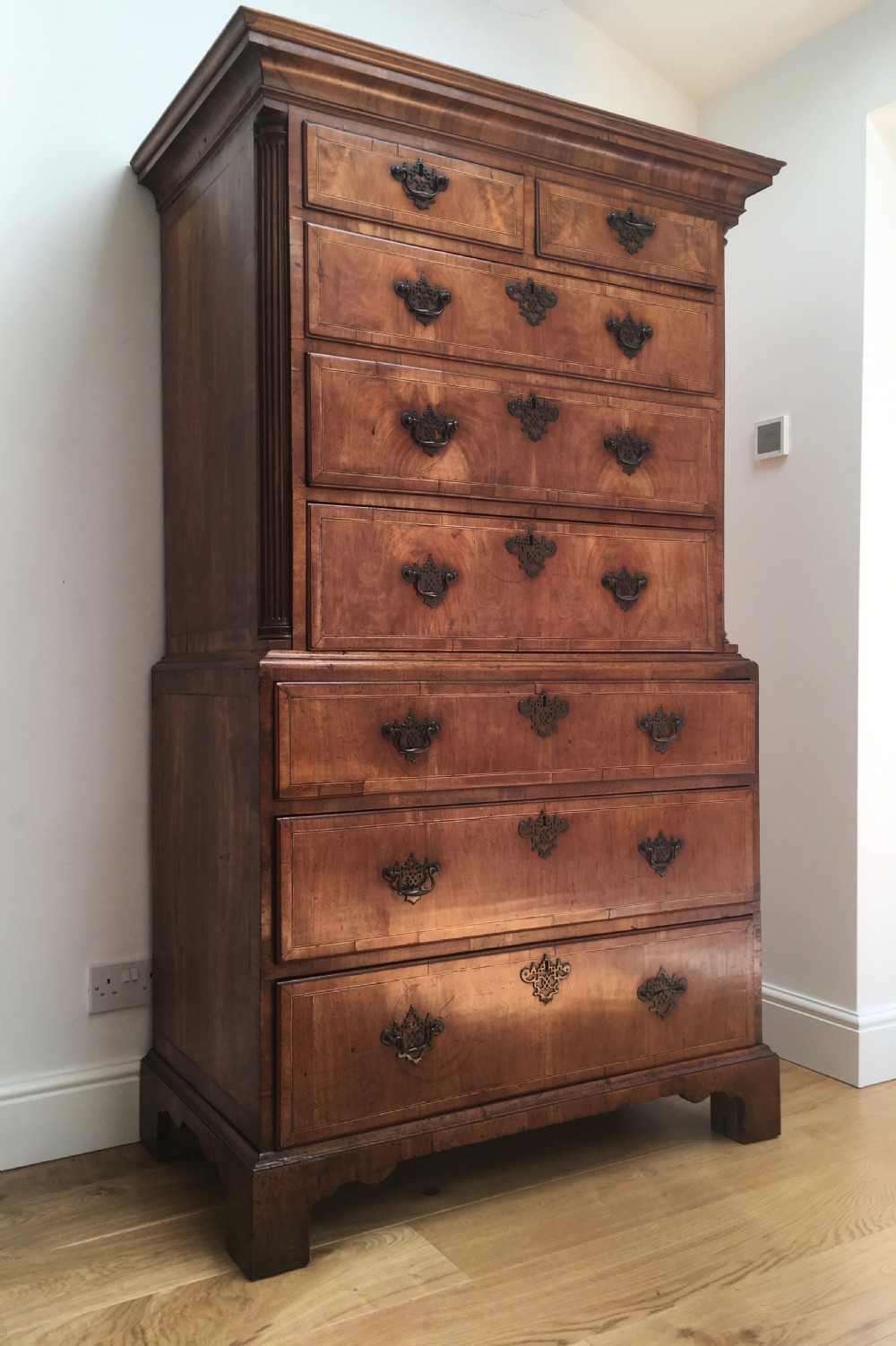 A George II walnut tallboy chest on chest featuring figured wood veneers, dark brass backplate handles, a moulded cornice, and bracket feet. View III