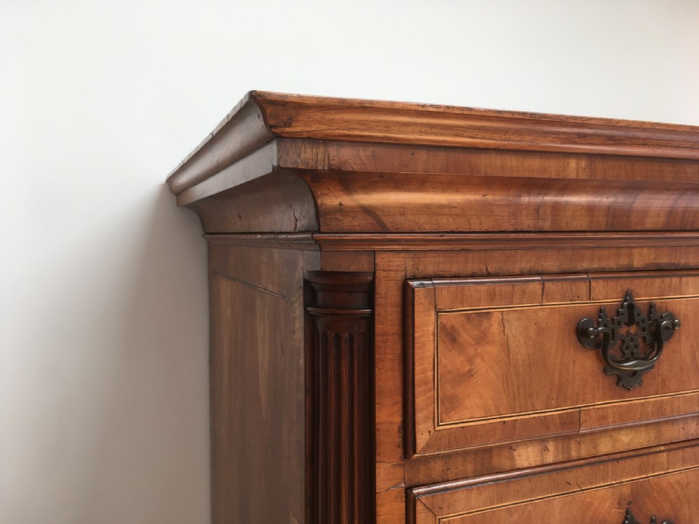 A George II walnut tallboy chest on chest featuring figured wood veneers, dark brass backplate handles, a moulded cornice, and bracket feet. View IV