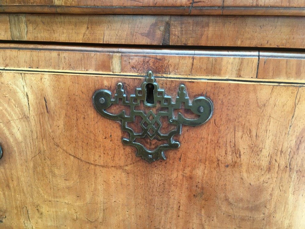 A George II walnut tallboy chest on chest featuring figured wood veneers, dark brass backplate handles, a moulded cornice, and bracket feet. View V