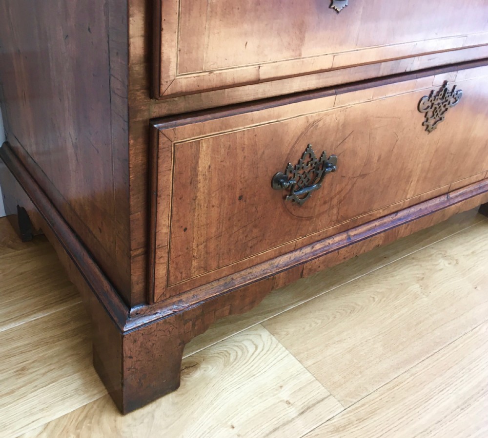 A George II walnut tallboy chest on chest featuring figured wood veneers, dark brass backplate handles, a moulded cornice, and bracket feet. View X