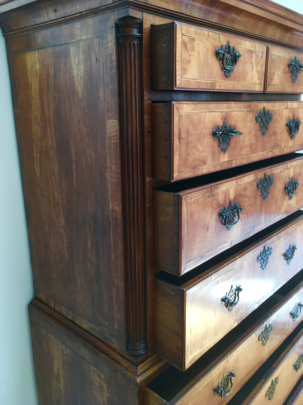 A George II walnut tallboy chest on chest featuring figured wood veneers, dark brass backplate handles, a moulded cornice, and bracket feet. View XII
