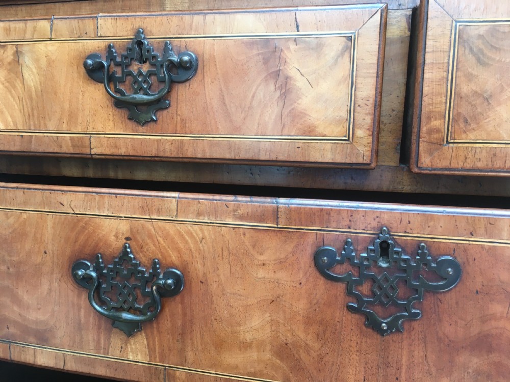 A George II walnut tallboy chest on chest featuring figured wood veneers, dark brass backplate handles, a moulded cornice, and bracket feet. View XV
